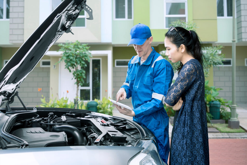 Image of Caucasian male mechanic checking broken car by using a tablet while talking to his client
